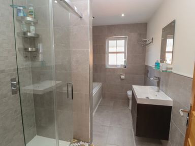 A bathroom with a glass shower, bathtub, toilet, and a sink with a mirror at 4 Centurion Rise in Penrith