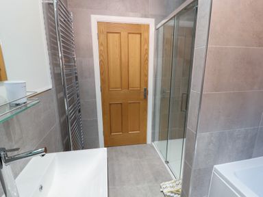 A bathroom with a wooden door a white sink a glass shower enclosure a towel radiator and a bathtub at 4 Centurion Rise in Penrith