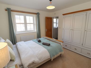 A bedroom with a double bed two rolled towels on it a large white wardrobe and a window with curtains at 4 Centurion Rise in Penrith