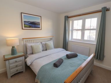 A bedroom with a bed with pillows and rolled towels a bedside table with a lamp and curtains on the window at 4 Centurion Rise in Penrith