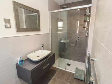 A bathroom with a wall-mounted sink, a framed mirror, a glass shower enclosure, and a towel on the floor at 4 Centurion Rise in Penrith