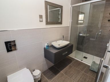 A bathroom with a wall-mounted sink and mirror next to a glass shower enclosure at 4 Centurion Rise in Penrith