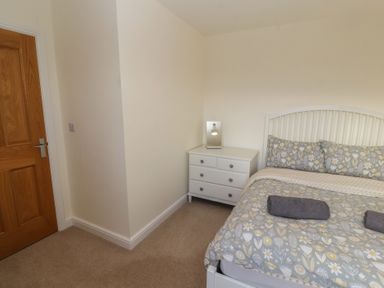 A bedroom with a bed with floral bedding a white nightstand with a lamp and a wooden door at 4 Centurion Rise in Penrith
