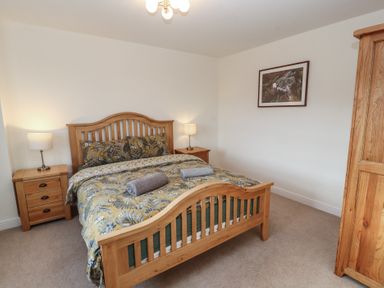 A bedroom with a wooden bed frame and matching bedside tables with lamps and a wardrobe at 4 Centurion Rise in Penrith