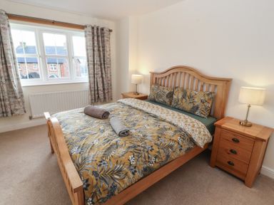 A bedroom with a wooden bed frame a floral duvet two bedside tables with lamps and curtains at 4 Centurion Rise in Penrith