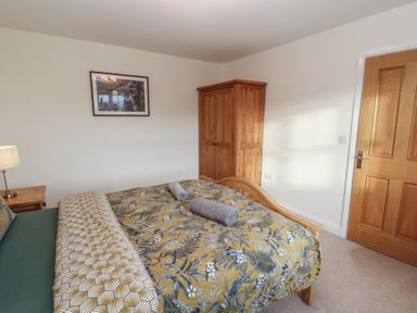 A bedroom with a wooden double bed covered with a floral bedspread and two rolled towels on top a wooden wardrobe a wooden door a side table with a lamp and a framed picture on the wall at 4 Centurion Rise in Penrith
