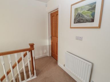 A hallway with a wooden door a radiator a staircase with white and wood balusters and a framed picture on the wall at 4 Centurion Rise Penrith
