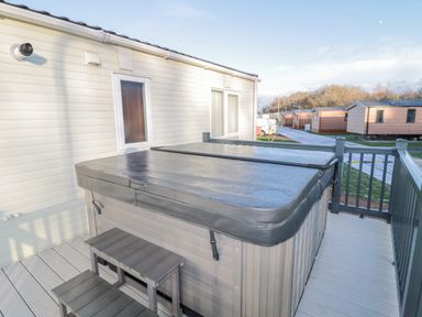A covered hot tub on a deck attached to a building with small stairs and other similar buildings nearby at Downtime Lodge near Felton