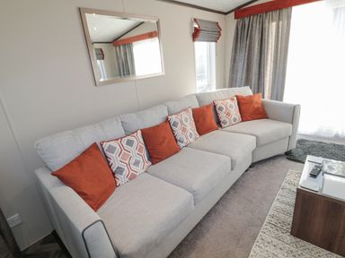 A living room with a light gray sofa with orange and patterned cushions near windows with gray curtains and a coffee table at Downtime Lodge near Felton
