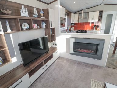 A living room with television and electric fireplace next to a kitchen with red backsplash at Downtime Lodge near Felton