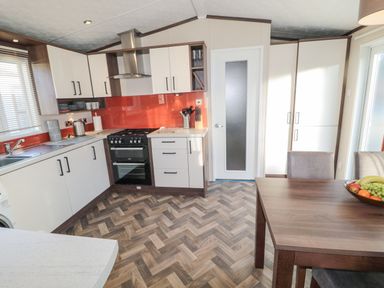 A kitchen with white cabinets a stove a dining table with chairs and a fruit bowl at Downtime Lodge near Felton