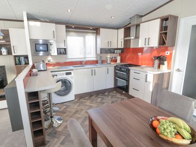 A kitchen with white cabinets a washing machine an oven microwave a dining table with fruit a breakfast bar and orange backsplash at Downtime Lodge near Felton