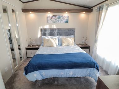 A bedroom with a bed blue bedding bedside tables lamps wardrobe with mirrored doors and curtains at Downtime Lodge near Felton