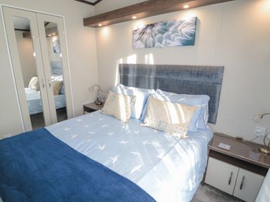 A bedroom with a bed a headboard bedside tables lamps and a mirrored wardrobe at Downtime Lodge near Felton