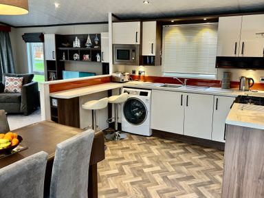 A kitchen with white cabinets washing machine microwave and two bar stools next to a dining table with chairs at Downtime Lodge near Felton