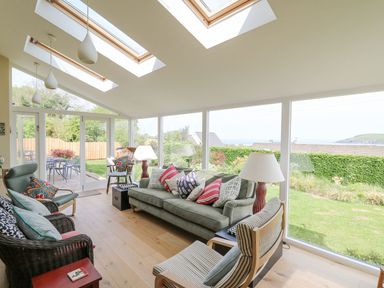 A sunroom with multiple chairs sofa and table lamps overlooking a garden at Tree Tops in Newport Pembrokeshire