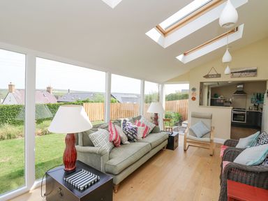 A lounge with a green sofa multiple cushions armchairs skylights and large windows overlooking a garden at Tree Tops in Newport Pembrokeshire