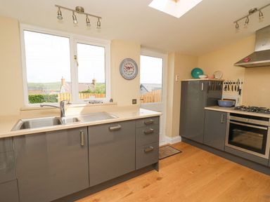 A kitchen with a sink under a window grey cabinets a stove and oven wooden floor and a door at Tree Tops Newport Pembrokeshire