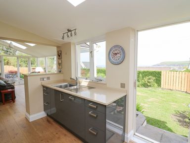 A kitchen with grey cabinets and a sink next to a door opening to a garden at Tree Tops in Newport Pembrokeshire