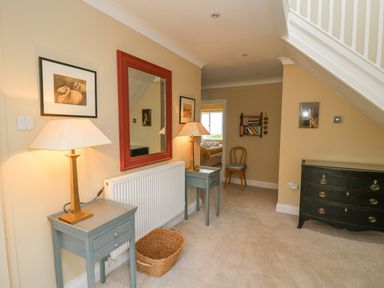 A hallway with two small tables and lamps a large mirror a wicker basket a wooden chair a bookshelf and a black chest of drawers at Tree Tops in Newport Pembrokeshire