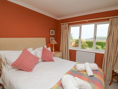 A bedroom with a bed with red patterned cushions and white sheets and towels on a blanket at Tree Tops in Newport Pembrokeshire