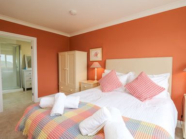 A bedroom with a bed with pillows and towels orange walls a wardrobe and an open door leading to a bathroom at Tree Tops in Newport Pembrokeshire