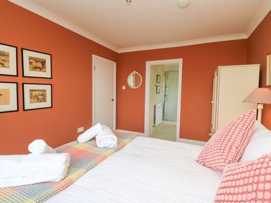 A bedroom with a bed with pink pillows white towels on a colorful blanket a wardrobe a lamp and pictures on the wall at Tree Tops in Newport Pembrokeshire