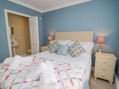 A bedroom with a bed with pillows bedside tables with lamps and an open door to a bathroom at Tree Tops in Newport Pembrokeshire