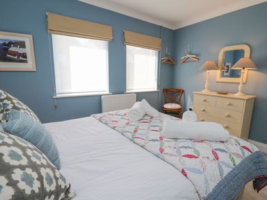 A bedroom with a bed with pillows and rolled towels a dresser with lamps and a mirror a chair and two windows at Tree Tops in Newport Pembrokeshire