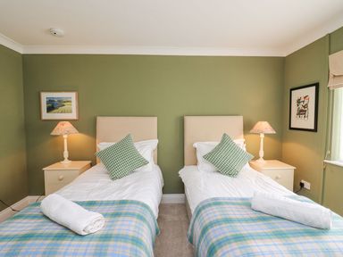 A bedroom with two single beds side by side each with a green pillow and a rolled towel on a plaid blanket at Tree Tops in Newport Pembrokeshire