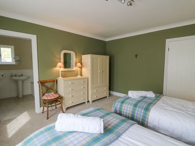 A bedroom with two single beds covered with blue and green plaid blankets and white towels with a wooden chair beside a cream dresser and wardrobe at Tree Tops in Newport Pembrokeshire