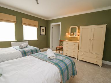 A bedroom with two single beds a dresser wardrobe chair and lamps at Tree Tops in Newport Pembrokeshire