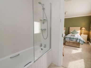 A bathroom with a bathtub and shower next to a bedroom with a bed and bedside table at Tree Tops in Newport Pembrokeshire
