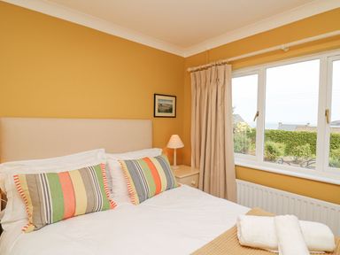 A bedroom with a double bed striped pillows bedside table lamp and window at Tree Tops in Newport Pembrokeshire