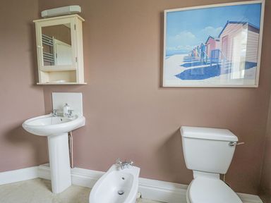 A bathroom with a sink bidet toilet mirror cabinet and beach huts art at Tree Tops in Newport Pembrokeshire