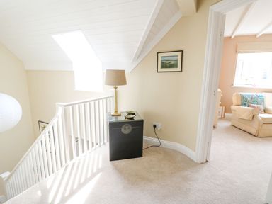 A hallway with a small table holding a lamp and two bowls near a staircase and an adjoining room with a chair at Tree Tops in Newport Pembrokeshire