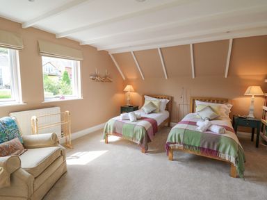 A bedroom with two single beds, armchair, side tables with lamps, and windows at Tree Tops in Newport Pembrokeshire