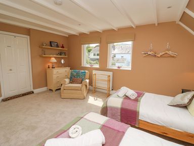 A bedroom with two single beds a beige armchair a chest of drawers and two windows at Tree Tops in Newport Pembrokeshire