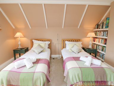 A bedroom with two single beds bedside tables with lamps and a bookshelf on the wall at Tree Tops in Newport Pembrokeshire