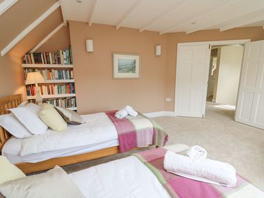 A bedroom with two single beds with pillows and blankets and a bookshelf with a lamp at Tree Tops in Newport Pembrokeshire