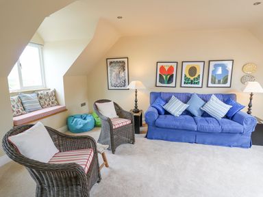 A living room with a blue sofa and wicker chairs near a window seat at Tree Tops in Newport Pembrokeshire