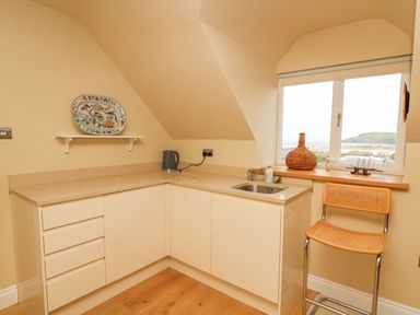 A small kitchen area with cream cabinets a countertop a sink a kettle a chair and a window with a coastal view at Tree Tops in Newport Pembrokeshire