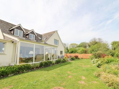 A house with a glass enclosed porch and a garden with grass and shrubs at Tree Tops in Newport Pembrokeshire