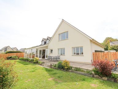 A large house with a glass sunroom patio and garden furniture in the backyard at Tree Tops in Newport Pembrokeshire