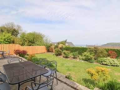 An outdoor patio with a metal table and chairs overlooking a garden with shrubs and grass at Tree Tops in Newport Pembrokeshire