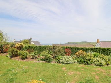 A garden with shrubs and bushes and a hedge overlooking houses and a distant hillside at Tree Tops in Newport Pembrokeshire