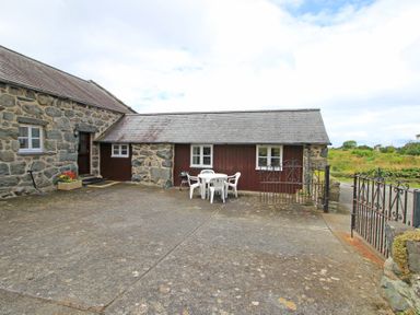 An outdoor patio with plastic table and chairs by a stone and wood building at Y Stabl The Old Stable in Llanbedr