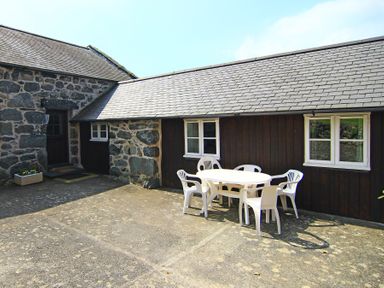 An outdoor patio area with a round white table and five white plastic chairs beside a stone and wood building at Y Stabl The Old Stable in Llanbedr