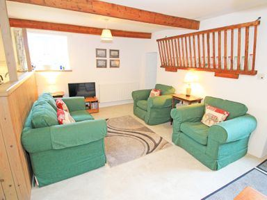 A living room with green sofas a rug a television and wooden beams at Y Stabl The Old Stable in Llanbedr