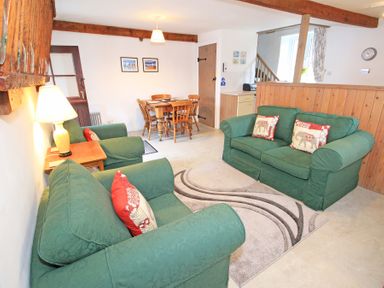 A living room with green sofas a wooden dining table and chairs and a wooden partition at Y Stabl The Old Stable in Llanbedr